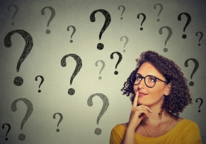 Thinking woman in glasses looking up at many question marks